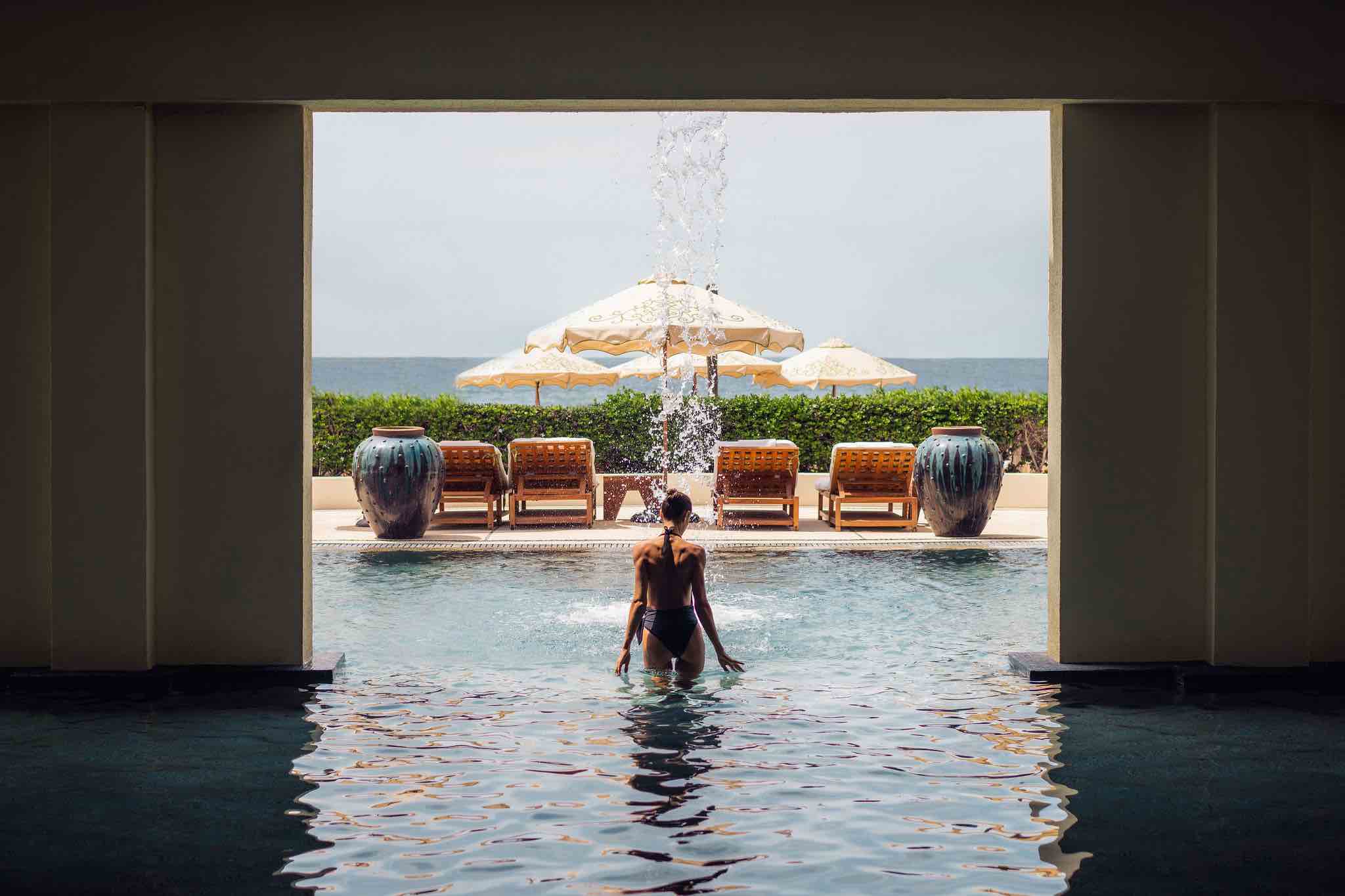 Indoor-outdoor wellness pool at a luxury Cabo San Lucas villa — a woman stepping from the indoor spa into the open-air pool with the Sea of Cortez in the background