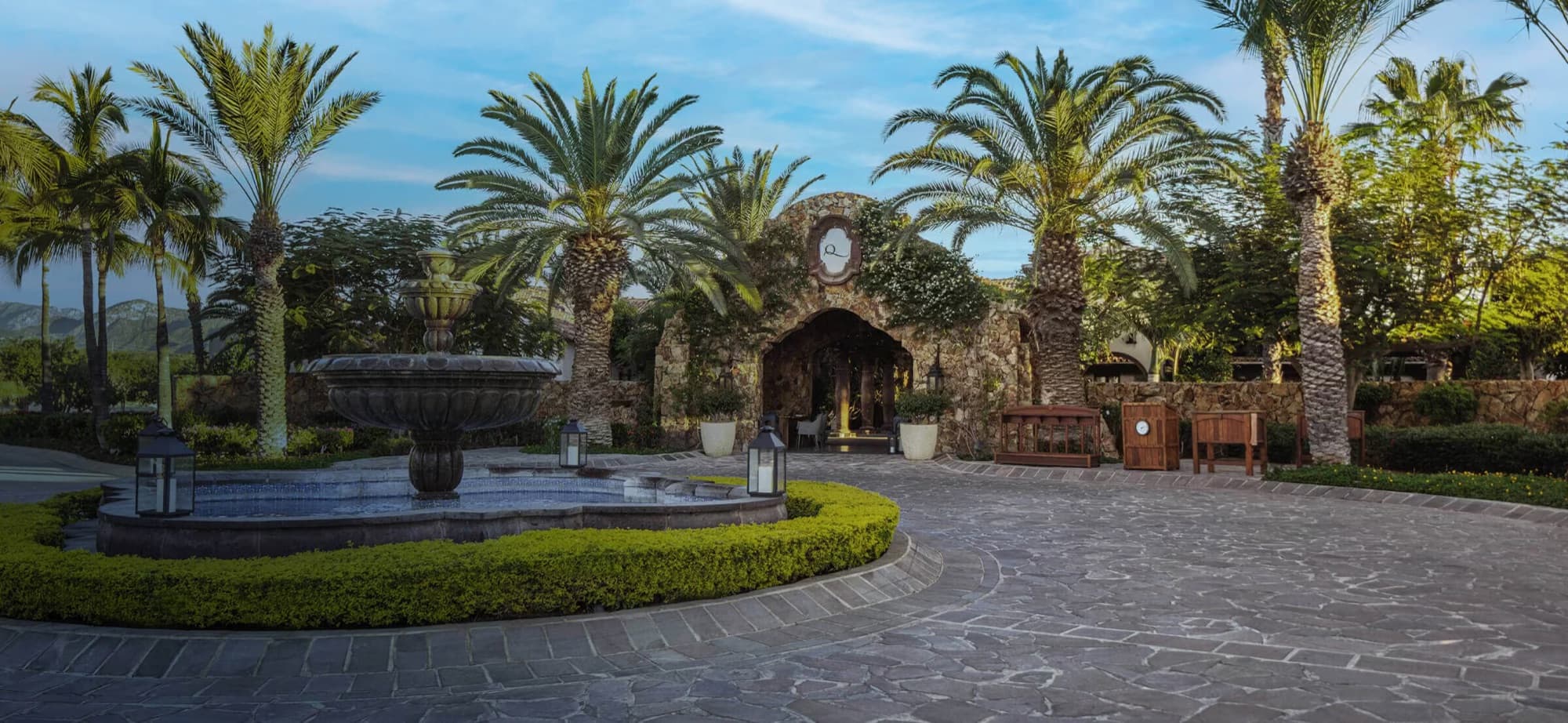 Palm-lined arrival court and stone gatehouse at the entrance to Querencia, Los Cabos